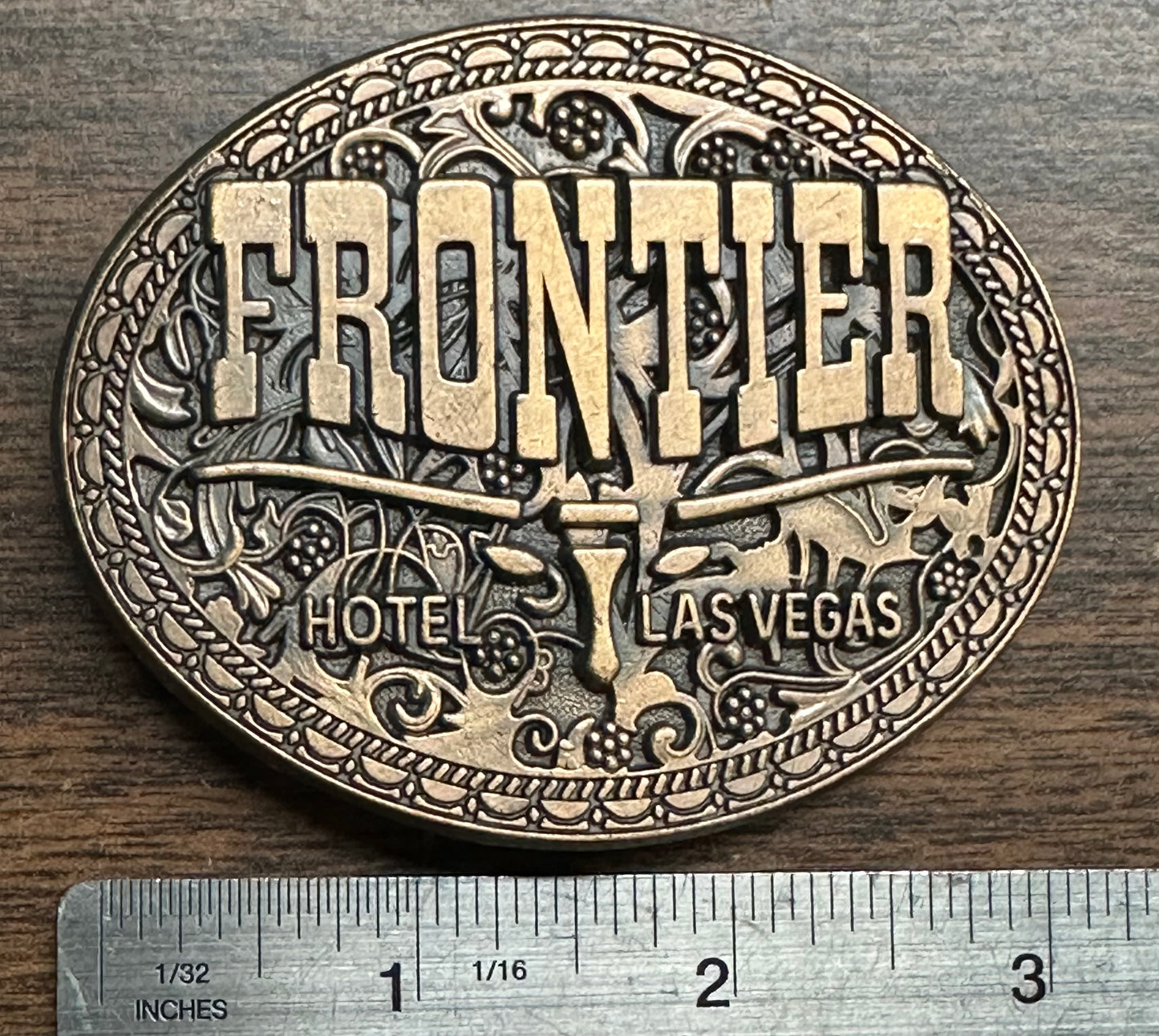 The Square Up Fashions Las Vegas Frontier Buckle is an oval vintage brass belt buckle with Western designs and "FRONTIER HOTEL LAS VEGAS" text, measuring about 3 inches wide.