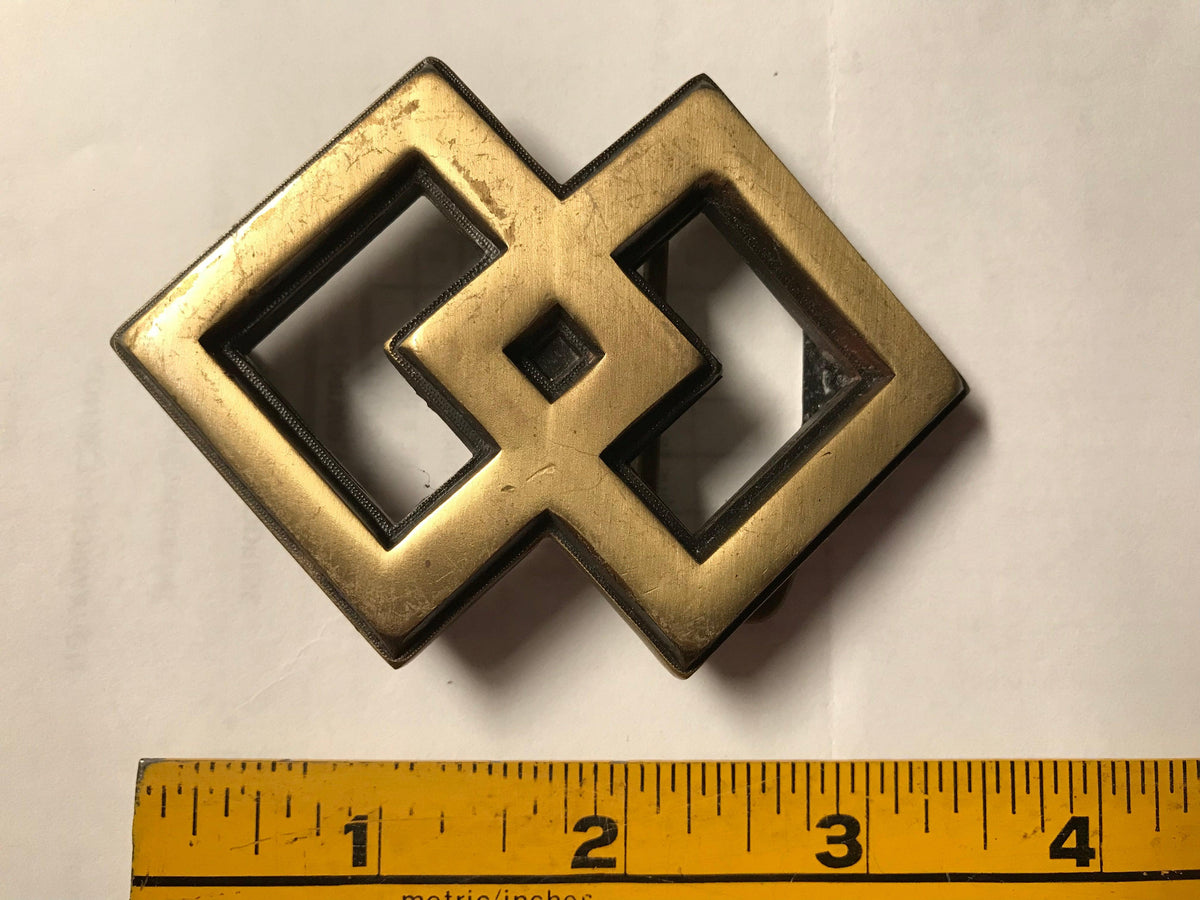 A Square Dance Buckle with an interlocking design, positioned next to a ruler, made by Square Up Fashions.