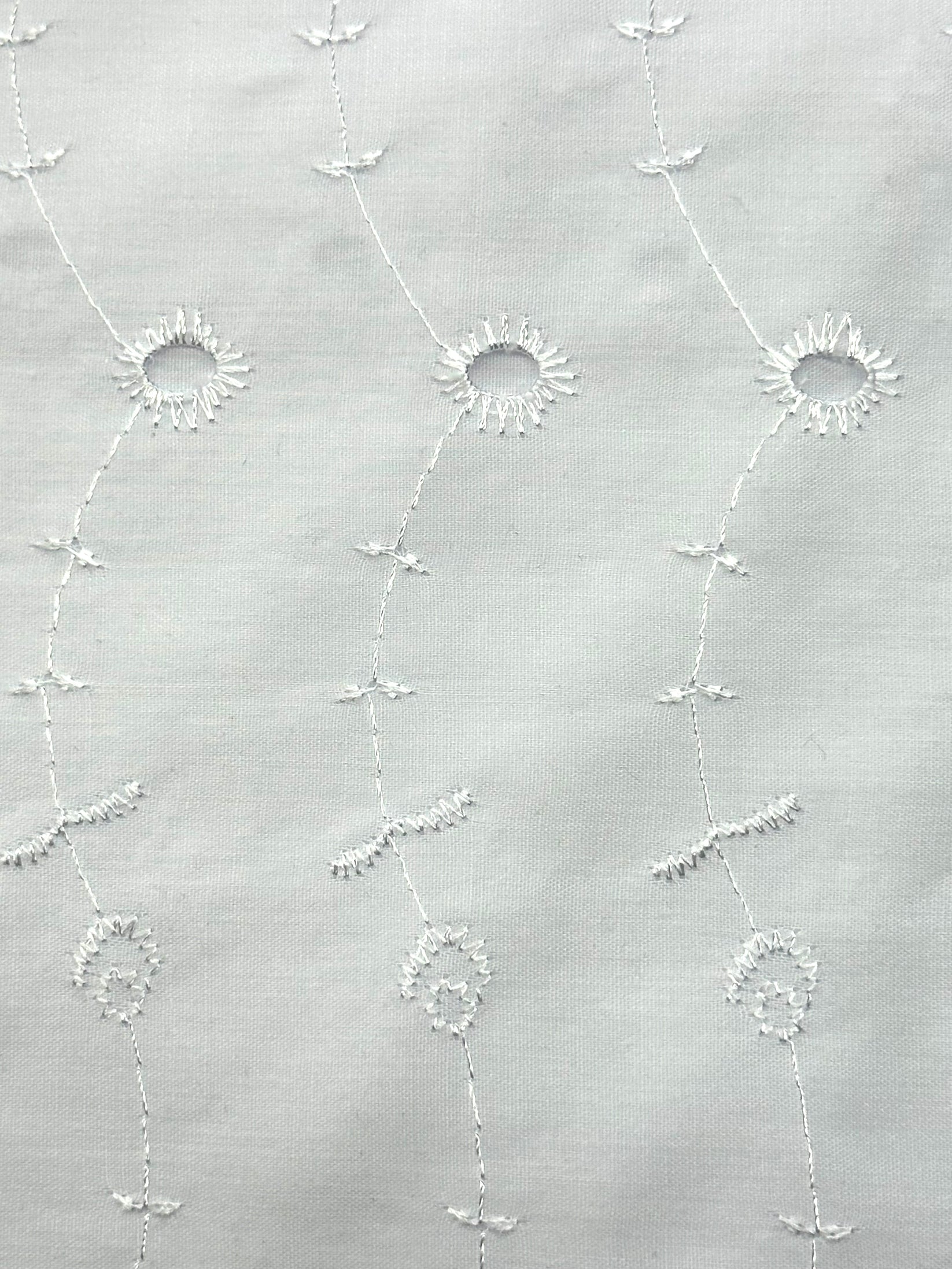 The 4 Tier Eyelet Prairie Skirt by Square Up Fashions features white fabric with embroidered circular floral patterns and curved lines, making it perfect for a lightweight summer look.