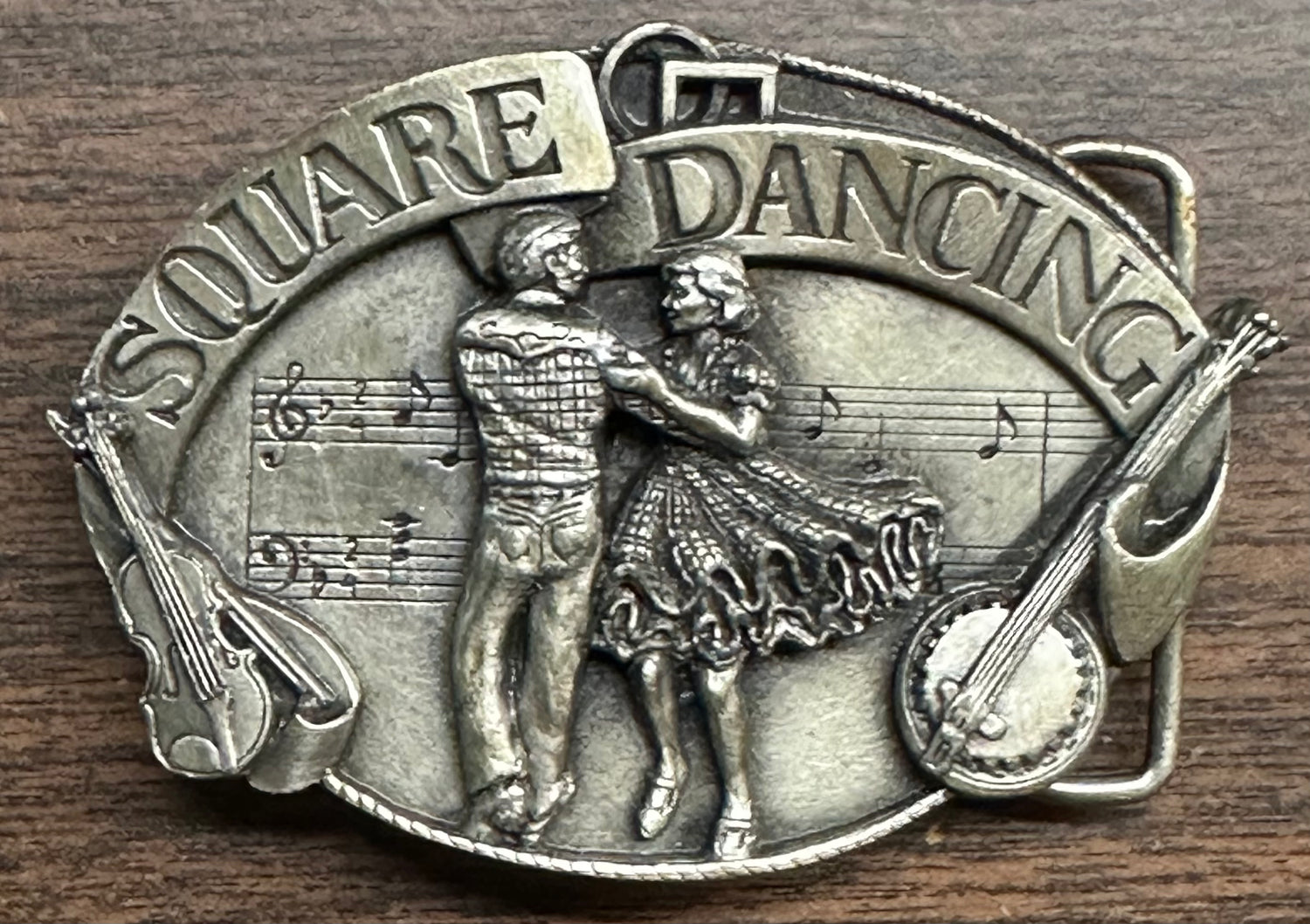 A vintage Square Dance Buckle w/ instruments by Square Up Fashions, depicting a dancing couple, musical notes, and "Square Dancing" at the top—a charming keepsake from the 1988 National Square Dance event.