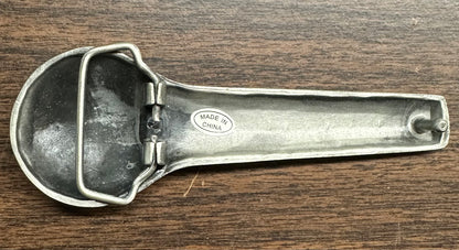 The SD Callers’ Belt Buckle by Square Up Fashions has a sturdy design that is reminiscent of a metal ice cream scoop with a hinged lever, complete with a “Made in China” label.