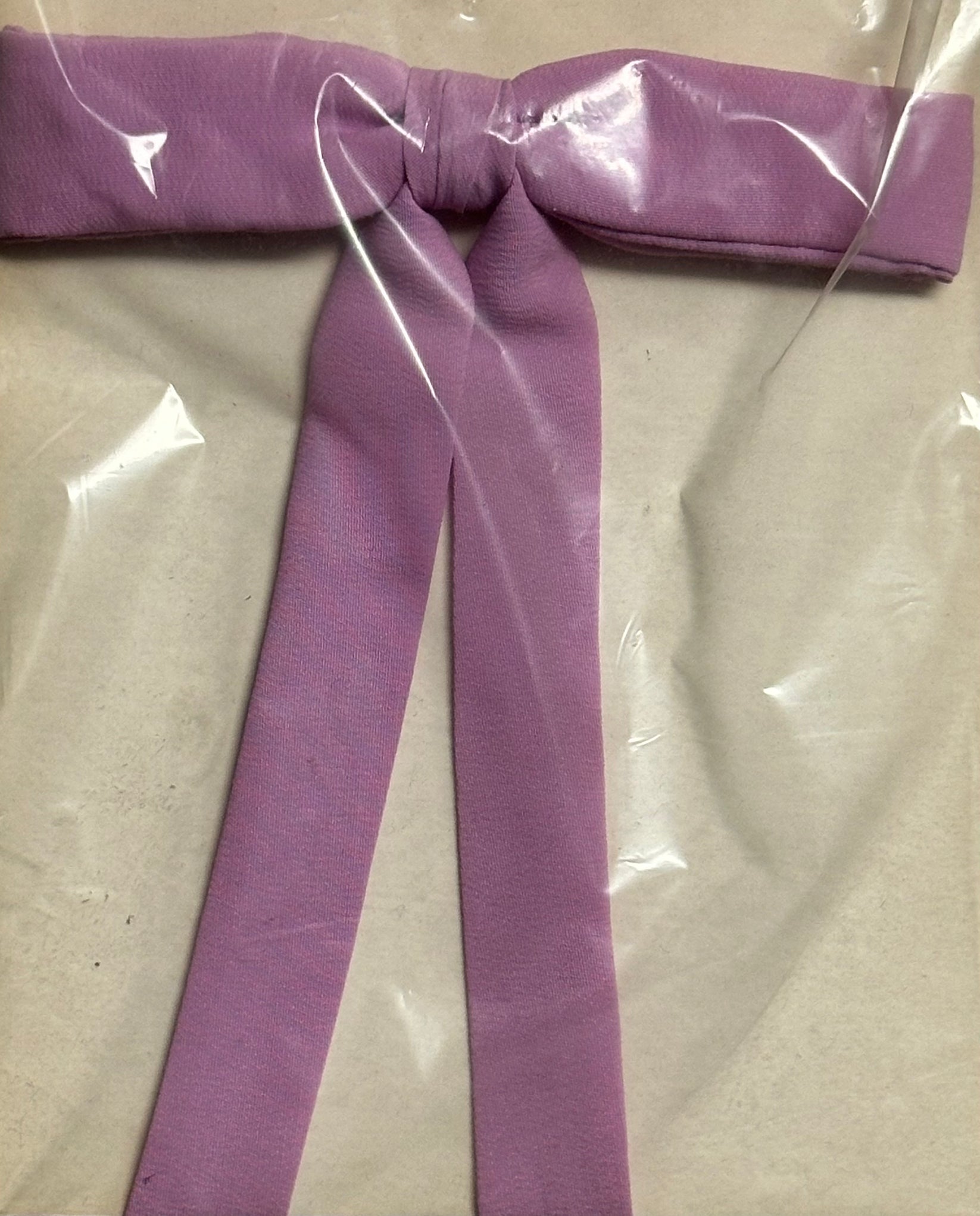 A Colonel Ties lavender fabric belt in a southern bow tie style from Square Up Fashions is showcased under clear plastic packaging on a simple background.