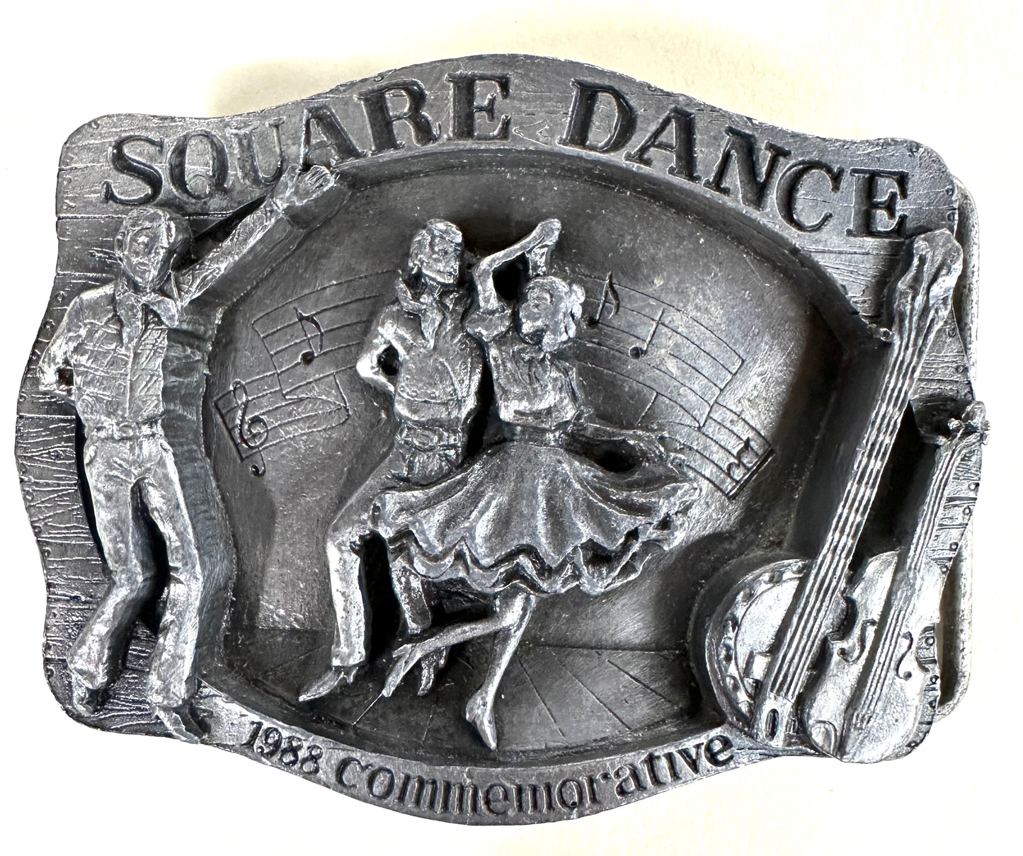 Square Up Fashions' "Square Dance Buckle w/ instruments"—a vintage metal plaque with dancers, musical notes, and double bass, commemorating the 1988 National Square Dance in Anaheim. Perfect for square dance collectors!.