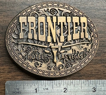 The Square Up Fashions Las Vegas Frontier Buckle is an oval vintage brass belt buckle with Western designs and "FRONTIER HOTEL LAS VEGAS" text, measuring about 3 inches wide.