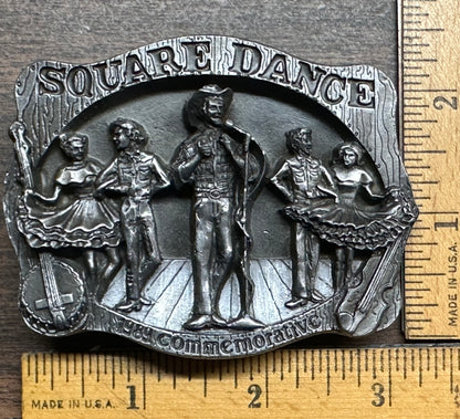 Square Up Fashions Square Dance Buckle w/caller features three dancing couples and "SQUARE DANCE" at the top. This 1989 commemorative buckle, made in USA, measures approx. 2.5 inches wide, as shown by the ruler.