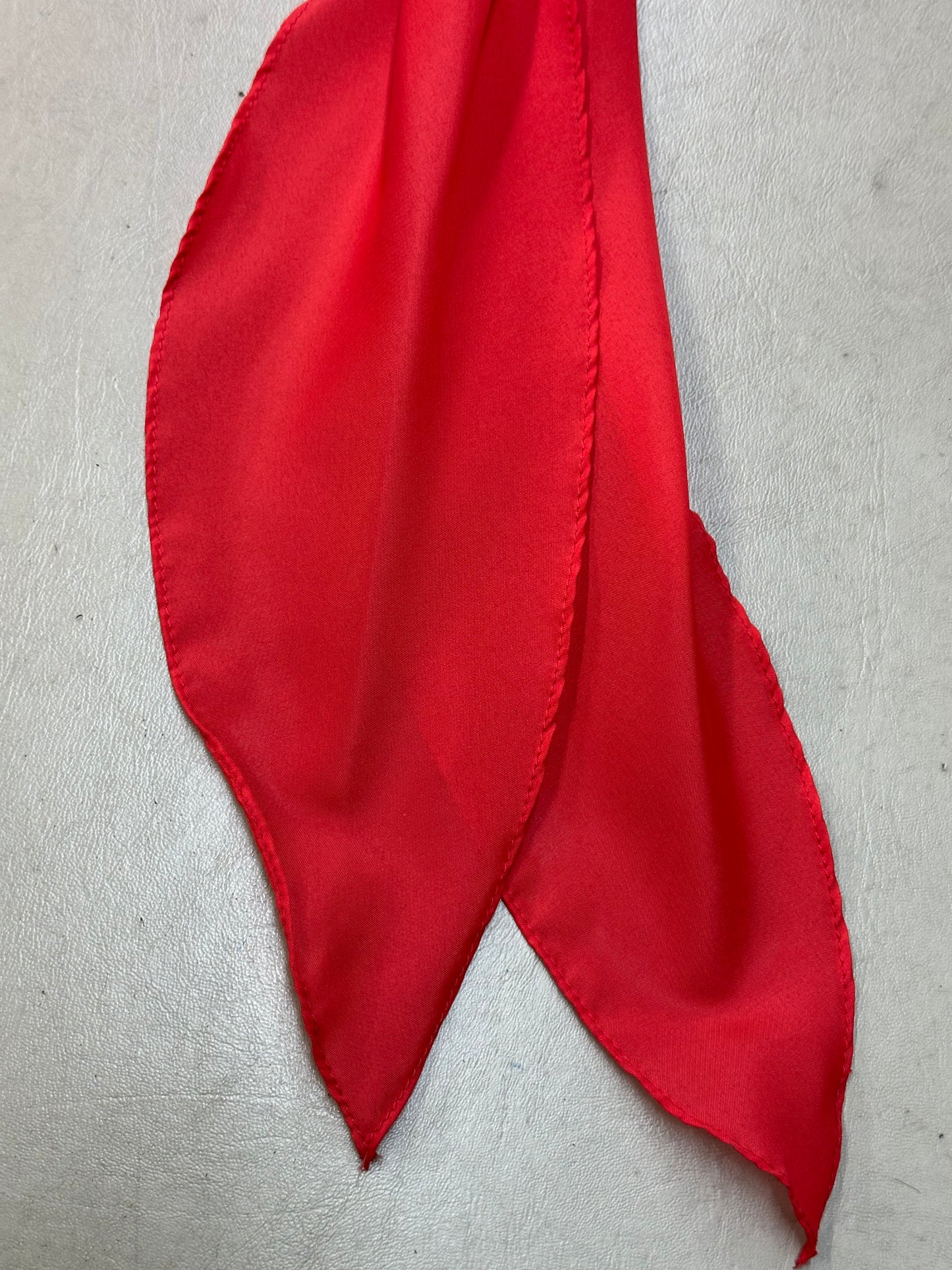 A close-up of the CLEARANCE Light Weight Thin Polyester Scarf Ties by Square Up Fashions highlights its vibrant red hue and jagged edges, displayed on a light surface, reflecting the style of soft, solid color ties.